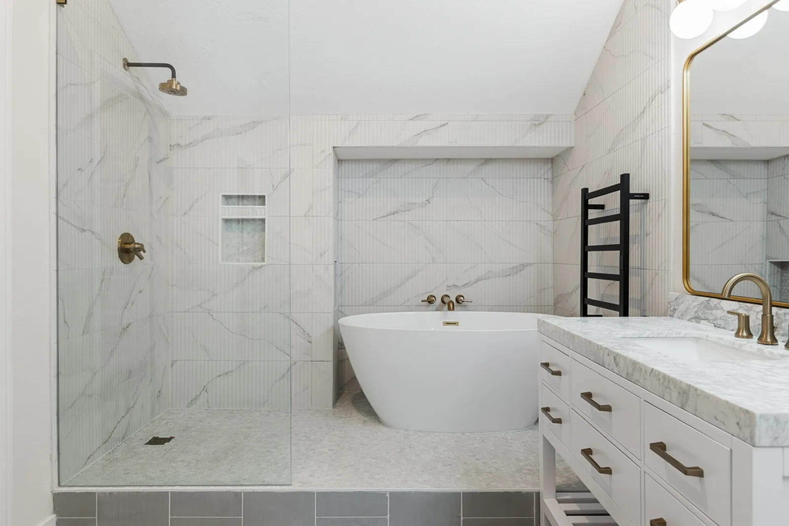 Primary bathroom at Azure Ln. in Addison after the pre-sale renovation: marble-look tile shower, freestanding tub, and white vanity with brass hardware