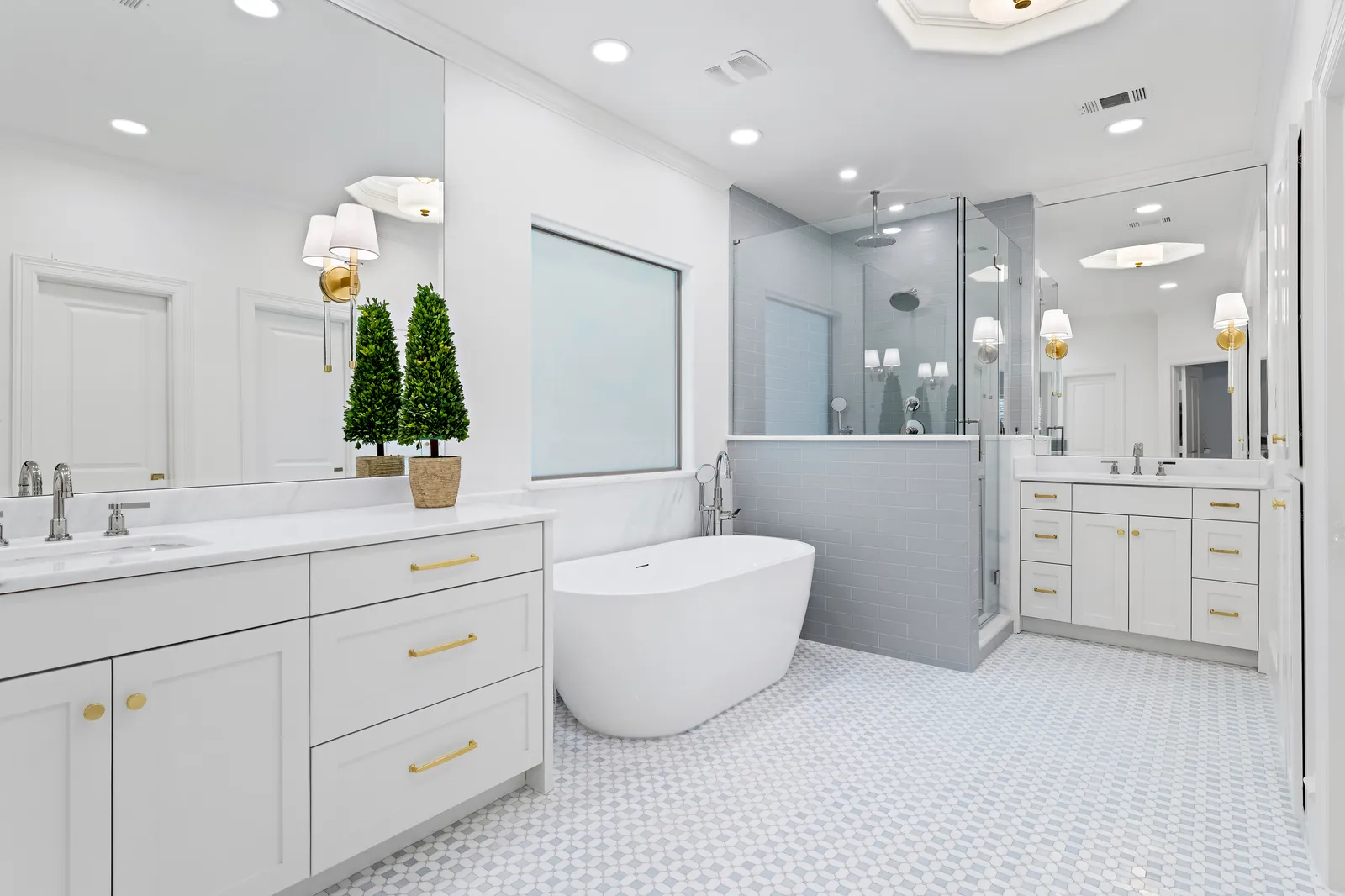 Primary bathroom at Revere Pl. in Lakewood: double vanities with brass hardware, freestanding tub, gray subway-tile shower with a half wall, and a mosaic tile floor