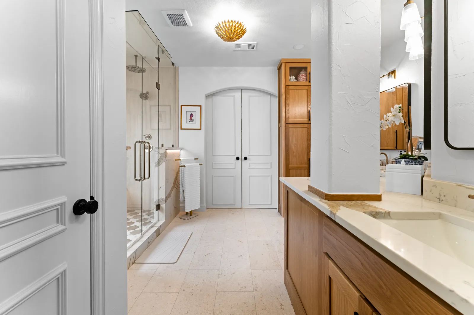 Primary bathroom at Shady Point Dr in Plano: glass shower, arched double doors, white oak cabinetry, and stone floors