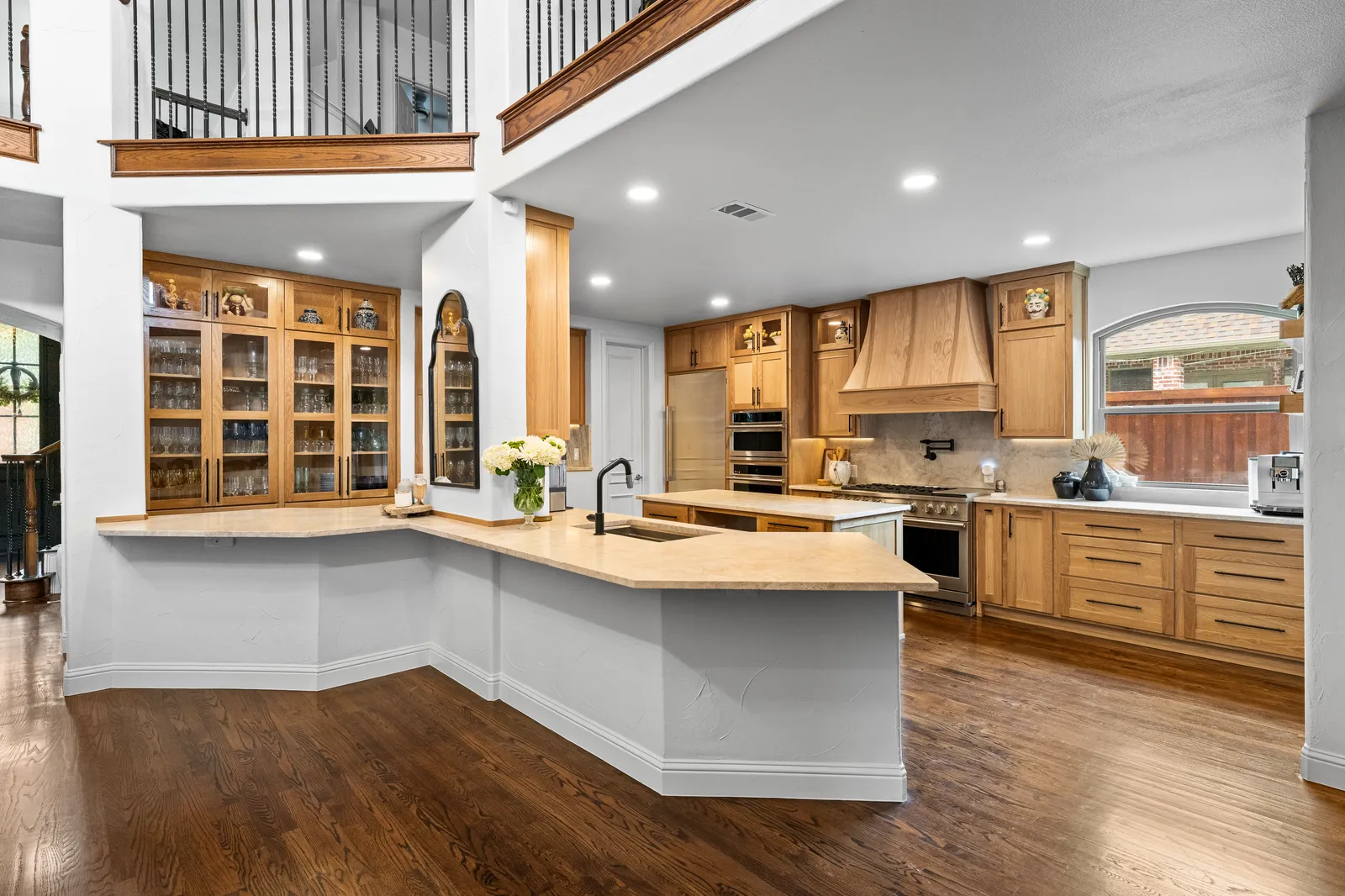 Remodeled kitchen at Shady Point Dr in Plano, TX by Renovation Sells Dallas: white oak cabinetry, plaster range hood, quartzite island, and refinished hardwood floors