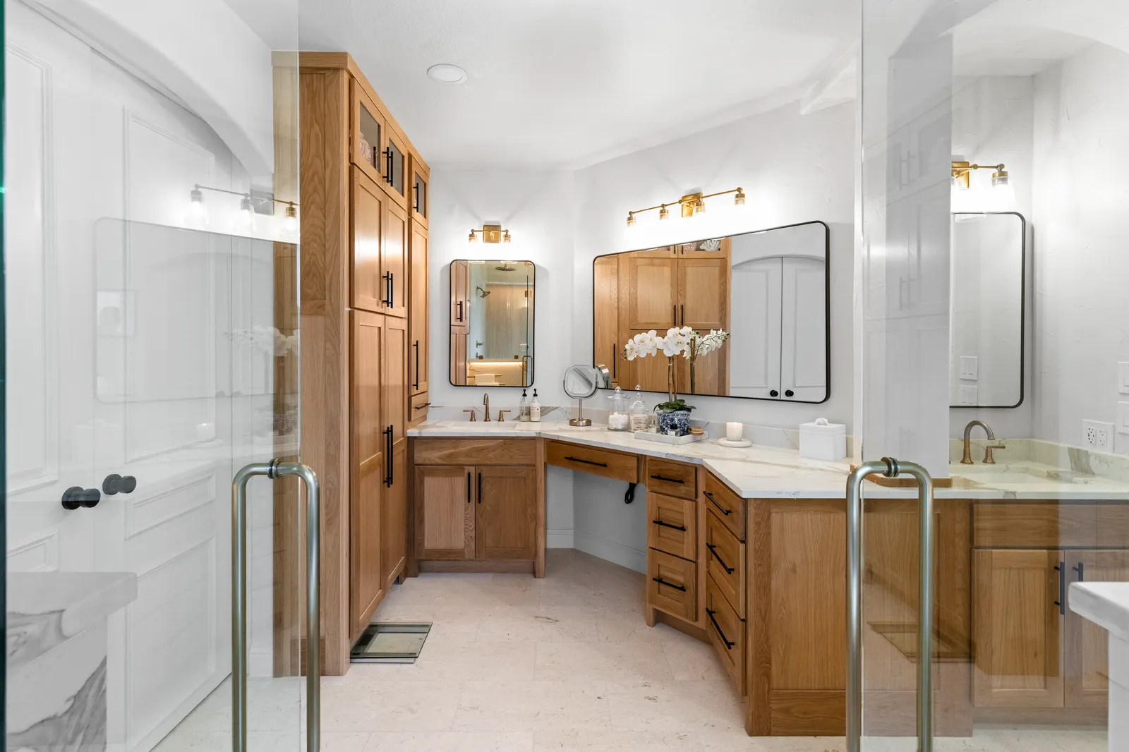 Primary bathroom vanity at Shady Point Dr in Plano after the remodel: white oak double vanity and tall cabinet, black-framed mirrors, brass sconces, and quartz counters